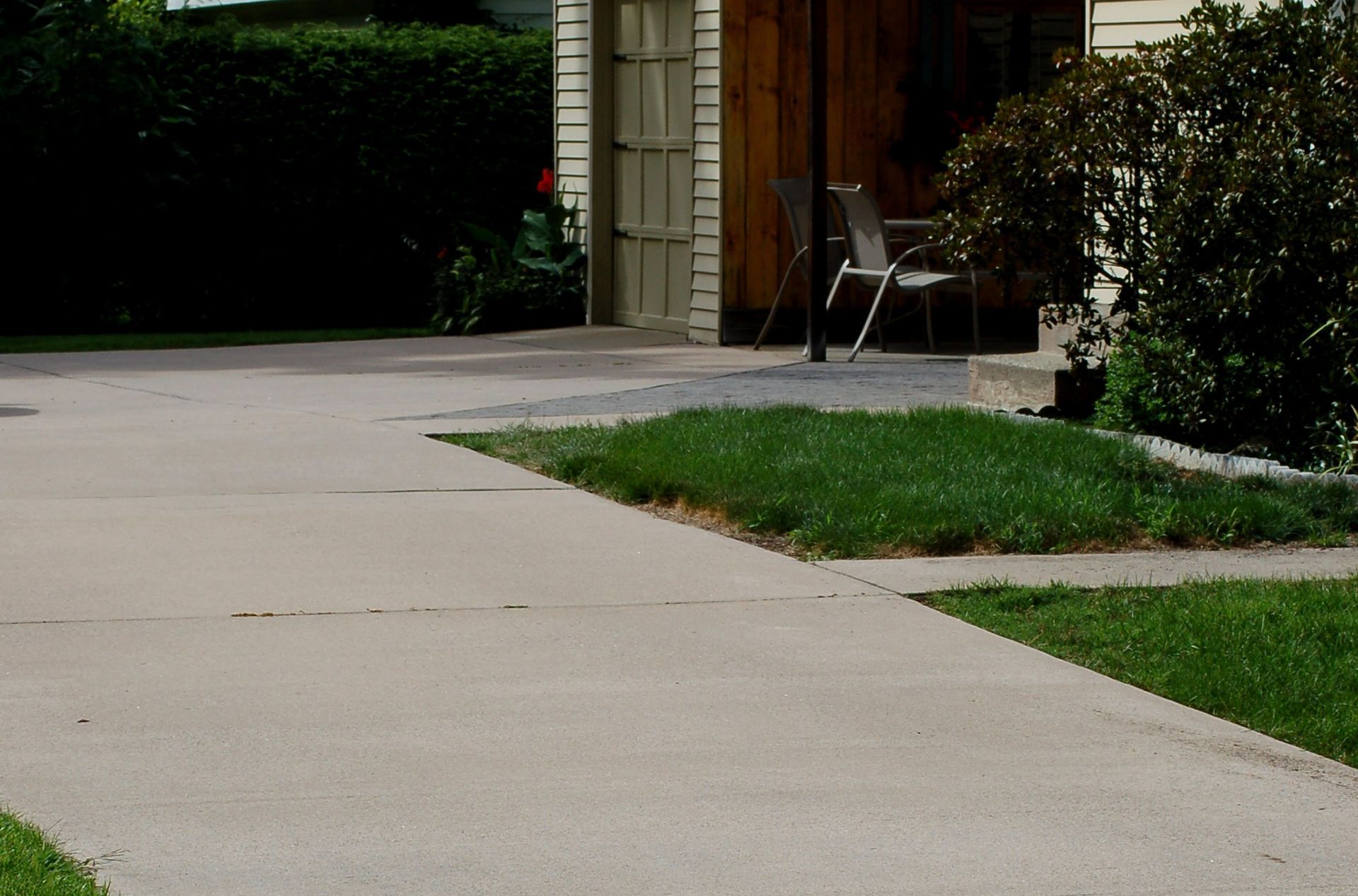 Driveway beside a house with a patch of grass and a chair near the garage.