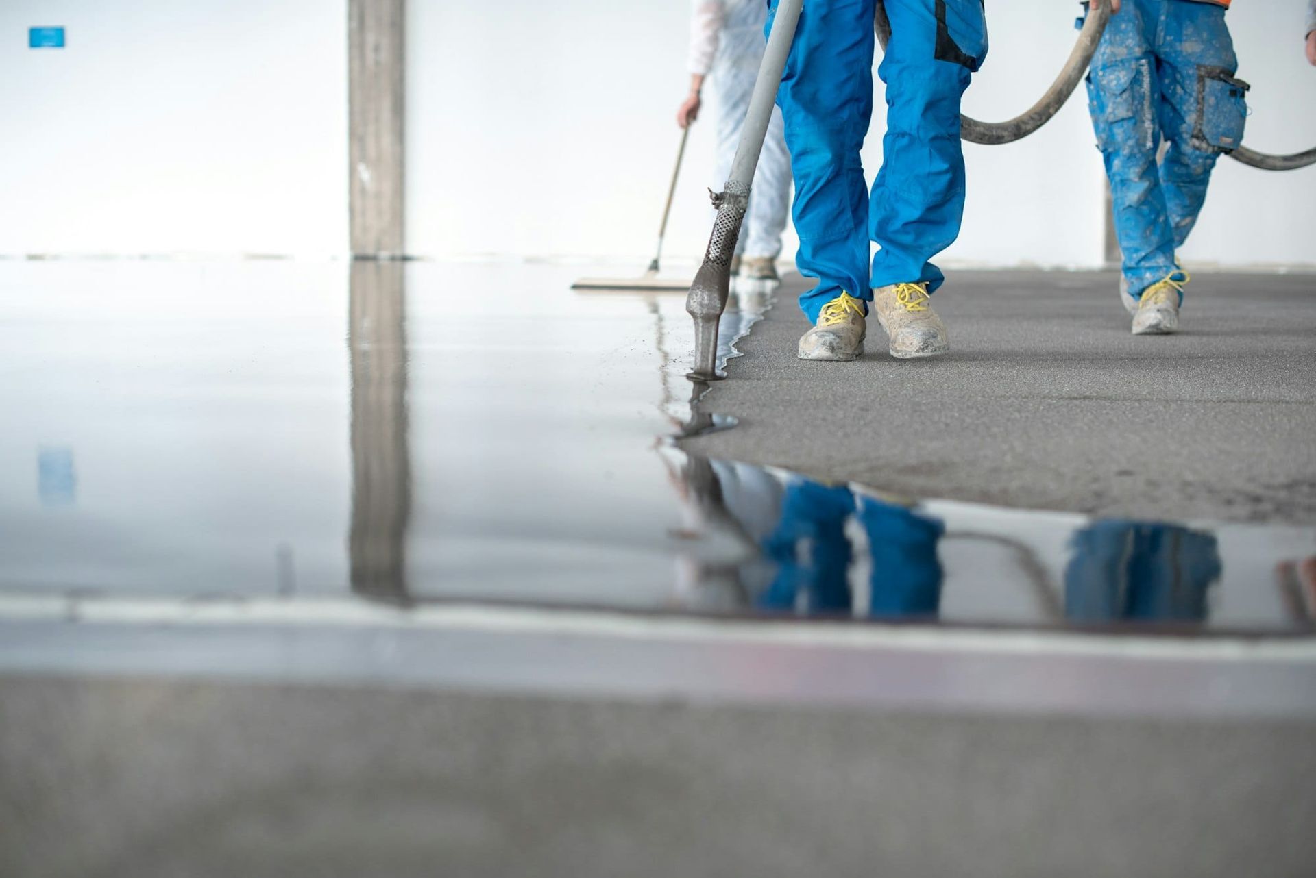 Workers in blue coveralls smoothing wet concrete on a floor surface