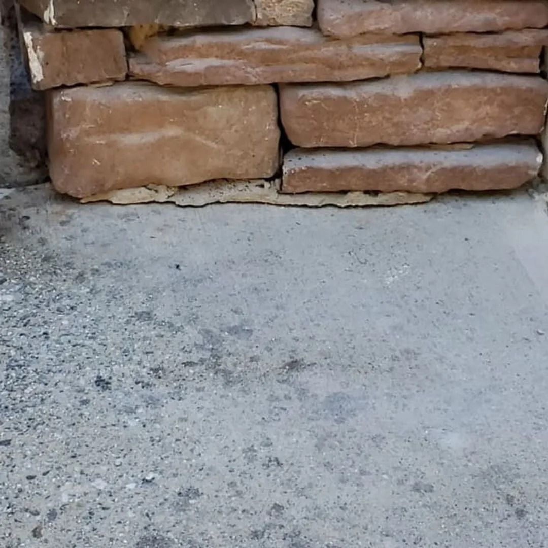 Stone wall above a light gray concrete floor with a rough, weathered texture