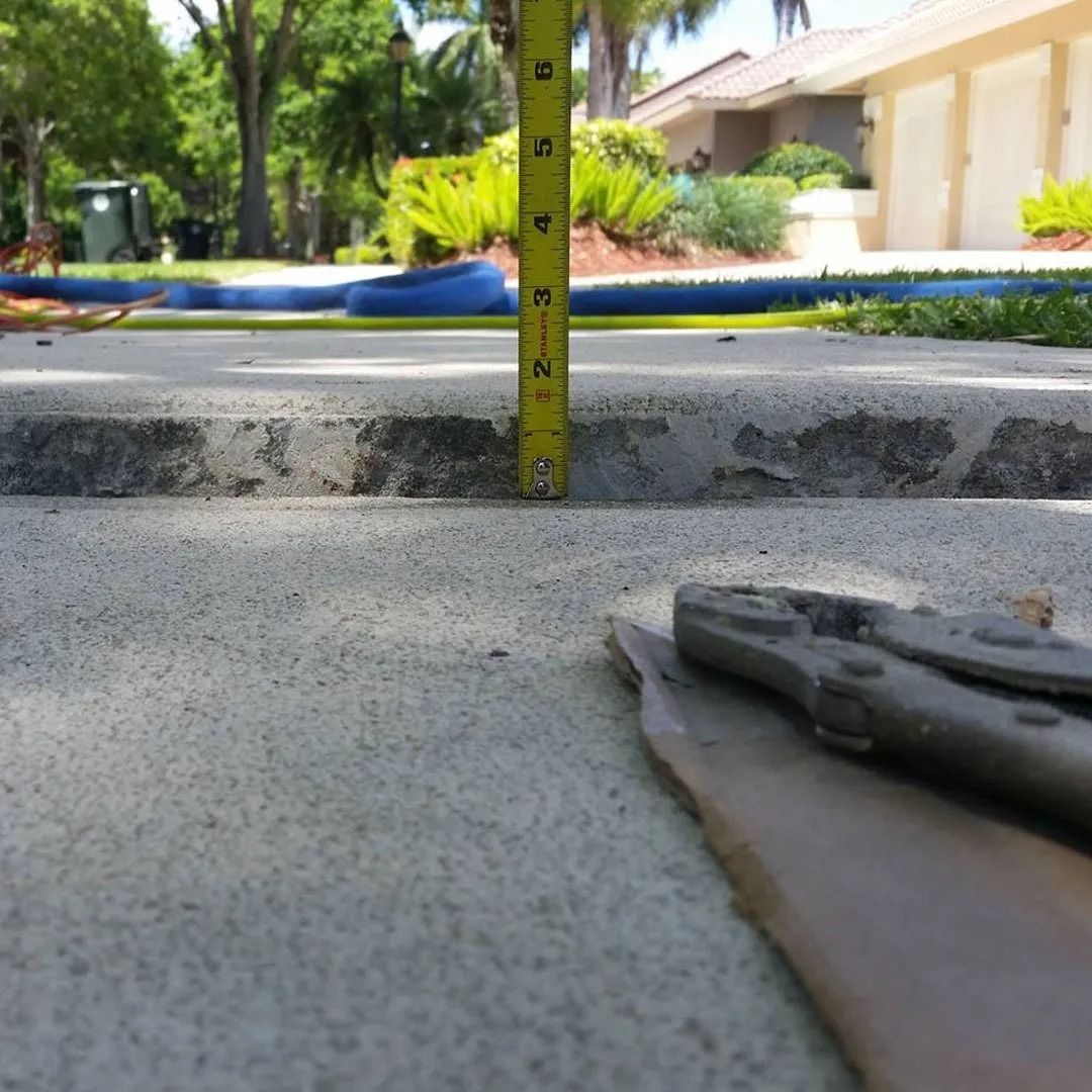 Measuring tape at curb level beside a concrete driveway, with a garden hose and house in the background