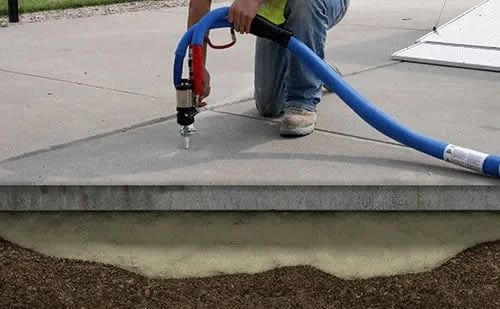 Worker cutting concrete sidewalk with a blue hose-connected saw during pavement repair