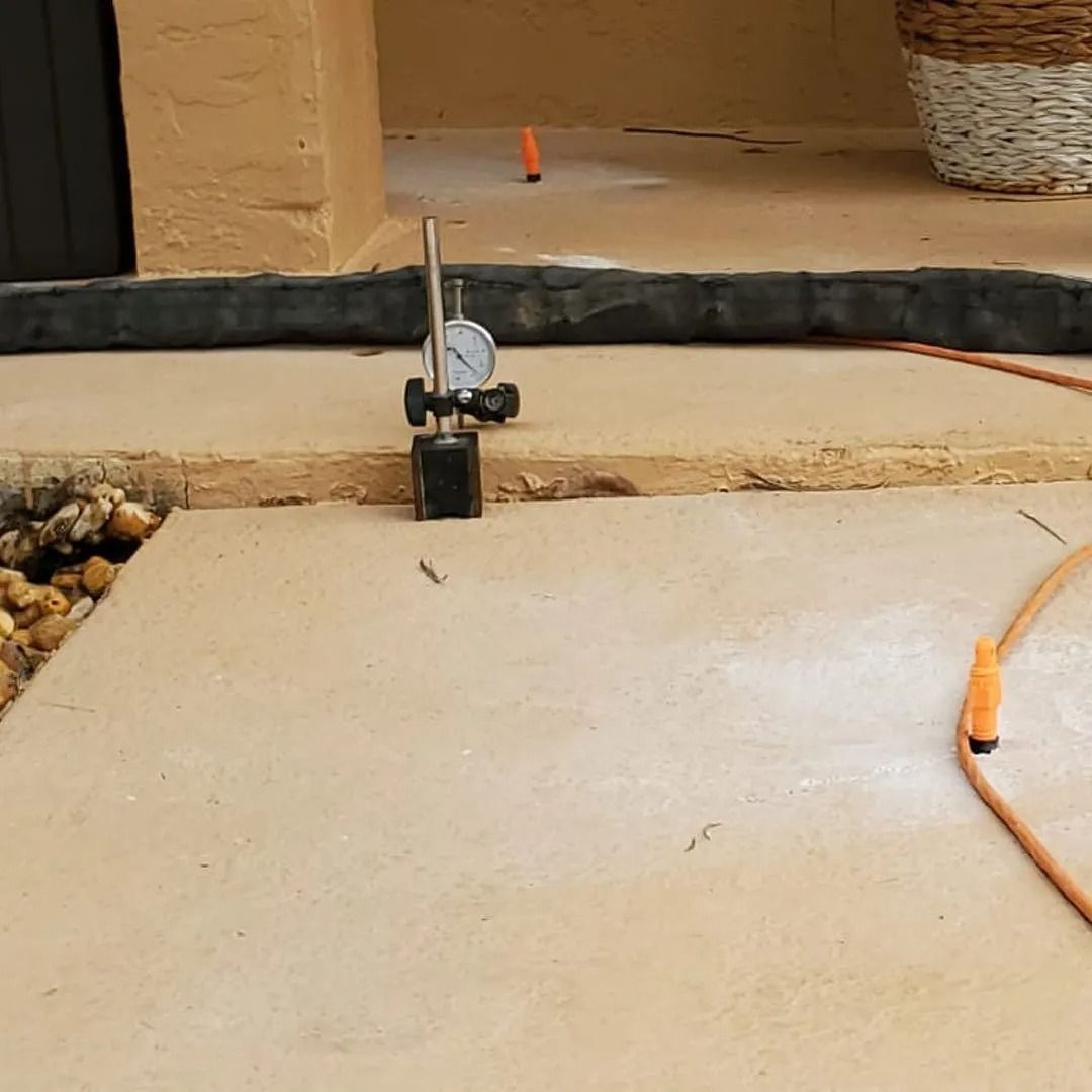 Small black-and-white cat peeking over a patio step near an orange cord