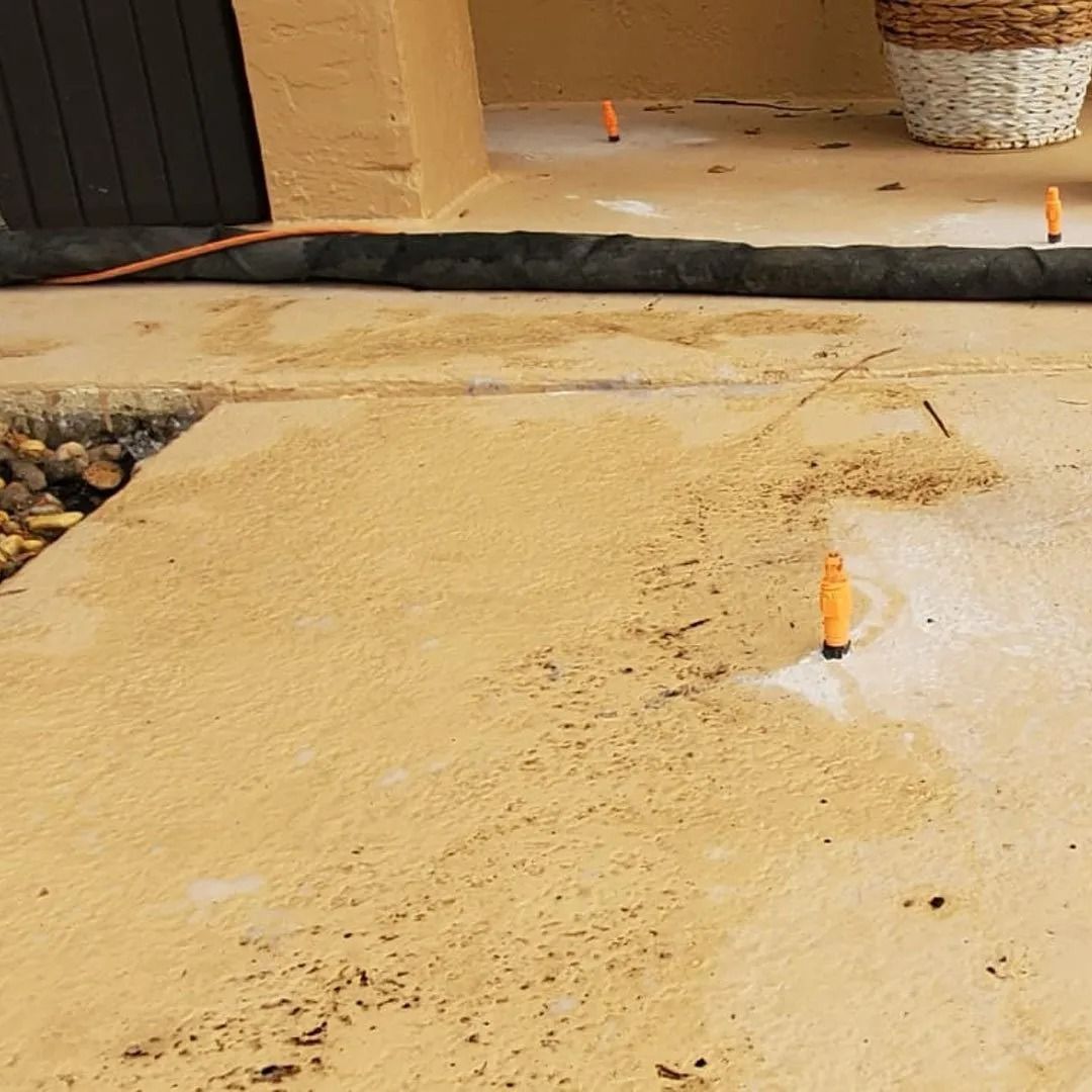 Tan concrete patio with orange markers and a black gate beside a rock border