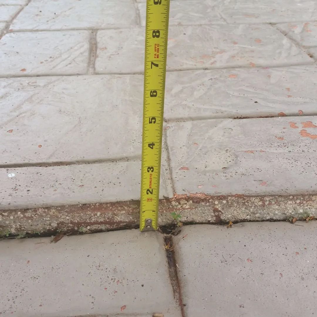 Yellow measuring tape standing on a concrete sidewalk step, showing the height of the curb.