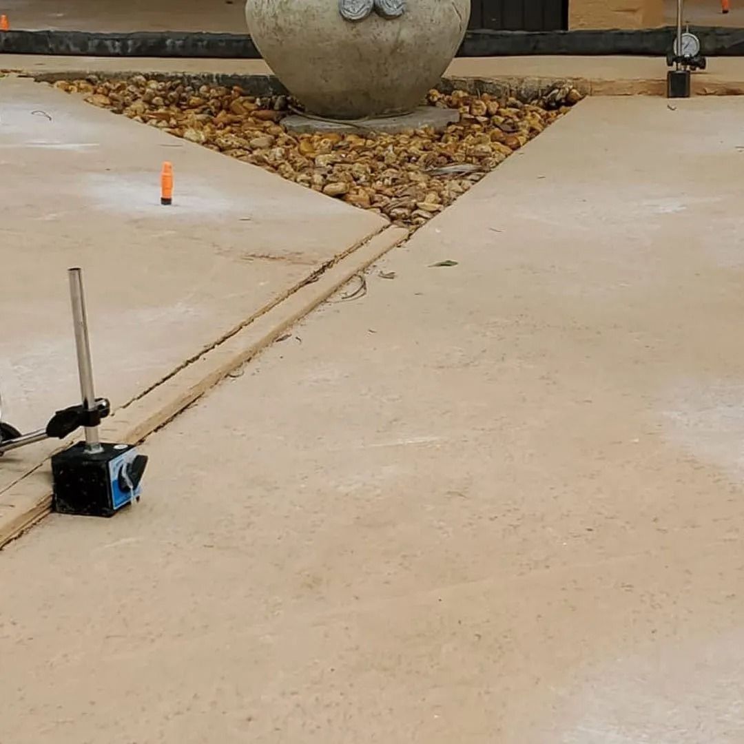 Blue device with antenna on a concrete sidewalk near a small orange marker and planter.
