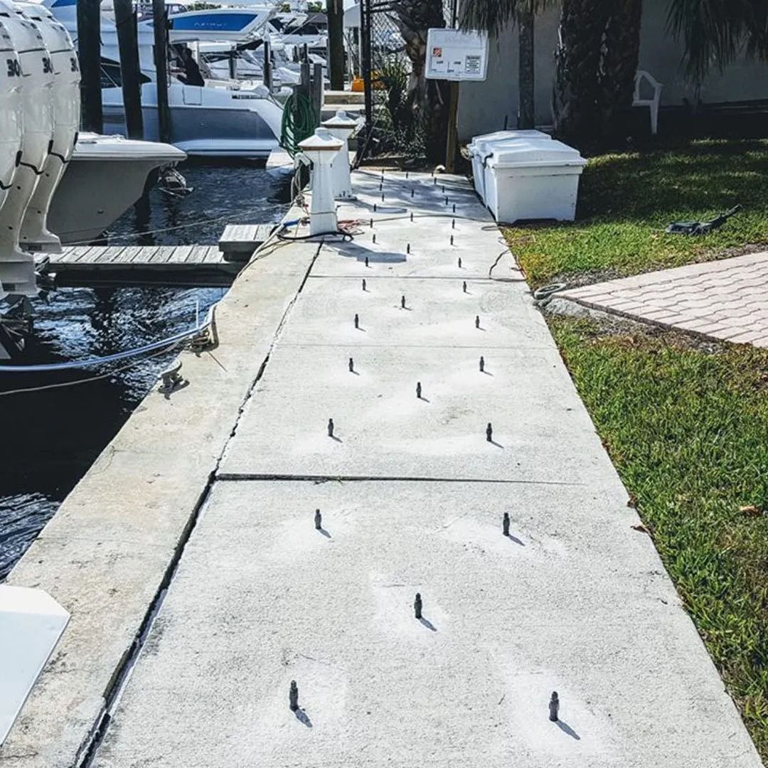 Concrete dock walkway beside boats and grass, with metal cleats along the path.