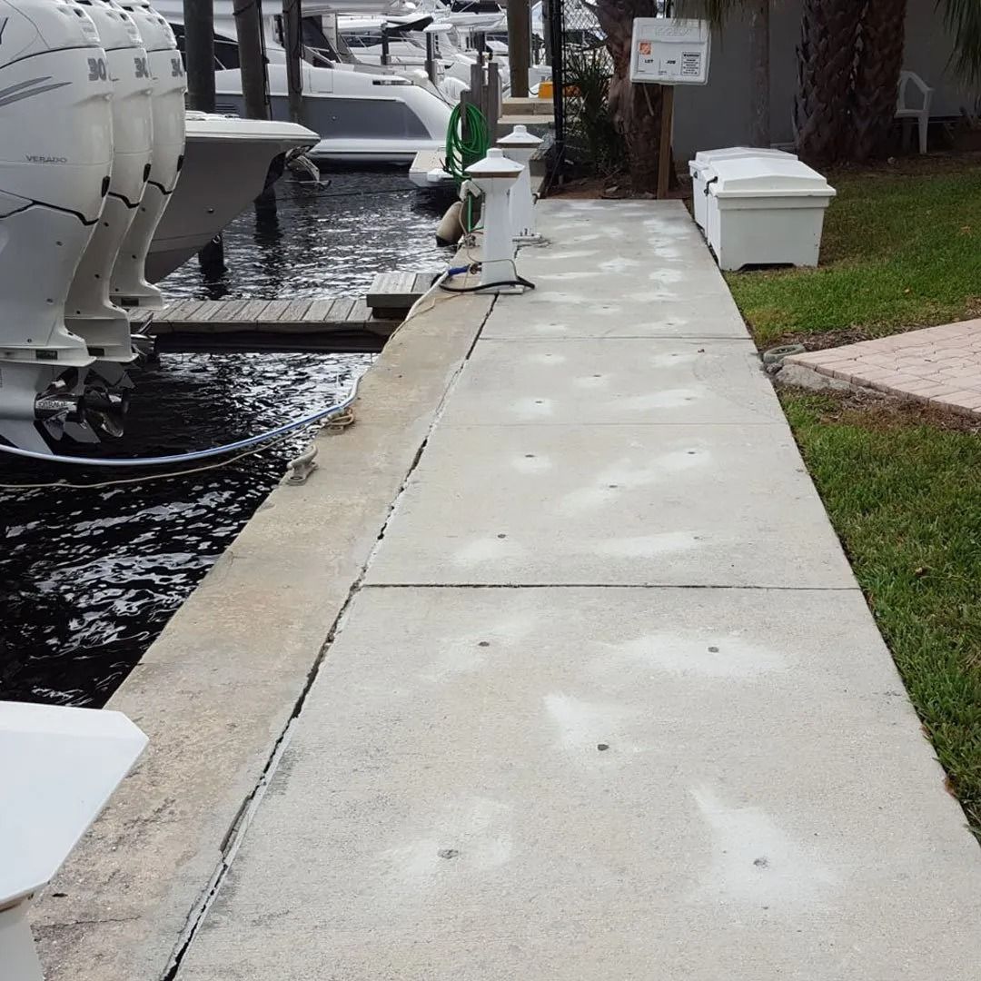 Concrete sidewalk beside a waterfront with white mooring posts and a wet curb on a cloudy day