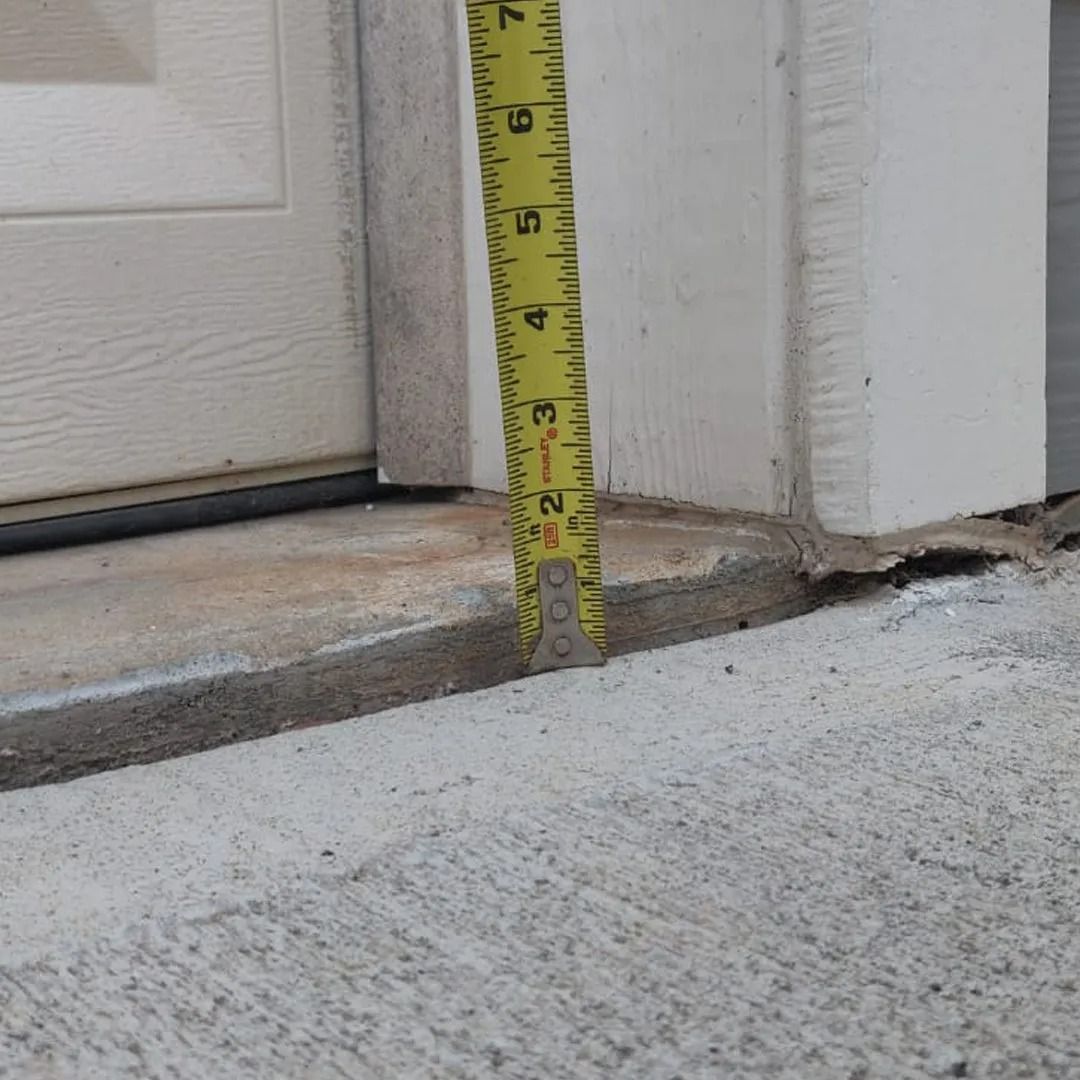 Tape measure showing a concrete step height beside a white door frame