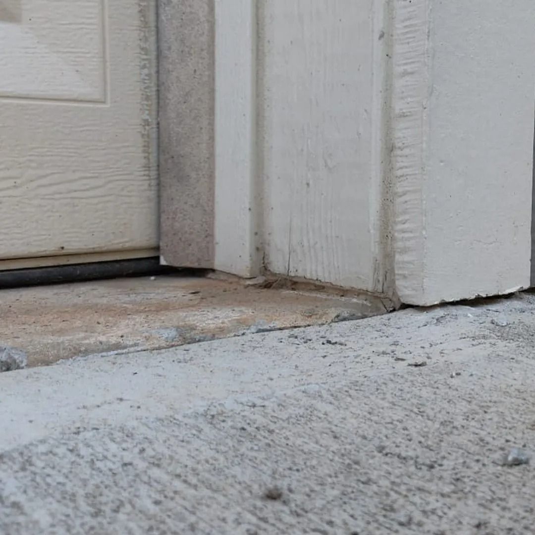 Close-up of a white door threshold with worn trim and concrete step.