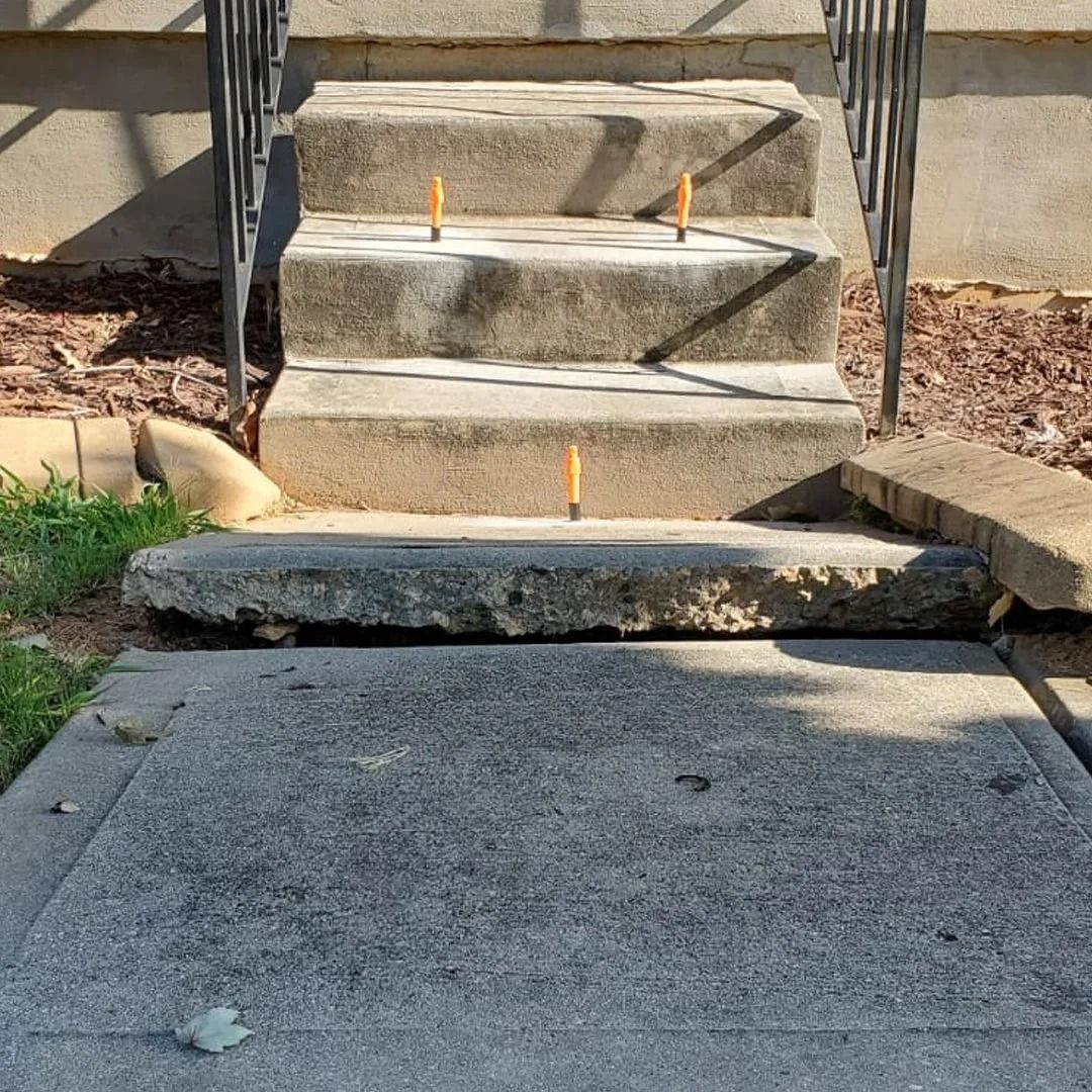 Concrete steps with small orange markers leading up from a driveway to a house entrance