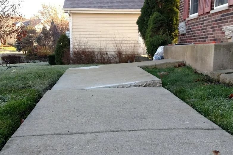 Concrete sidewalk with a raised, uneven patch beside a house and garage