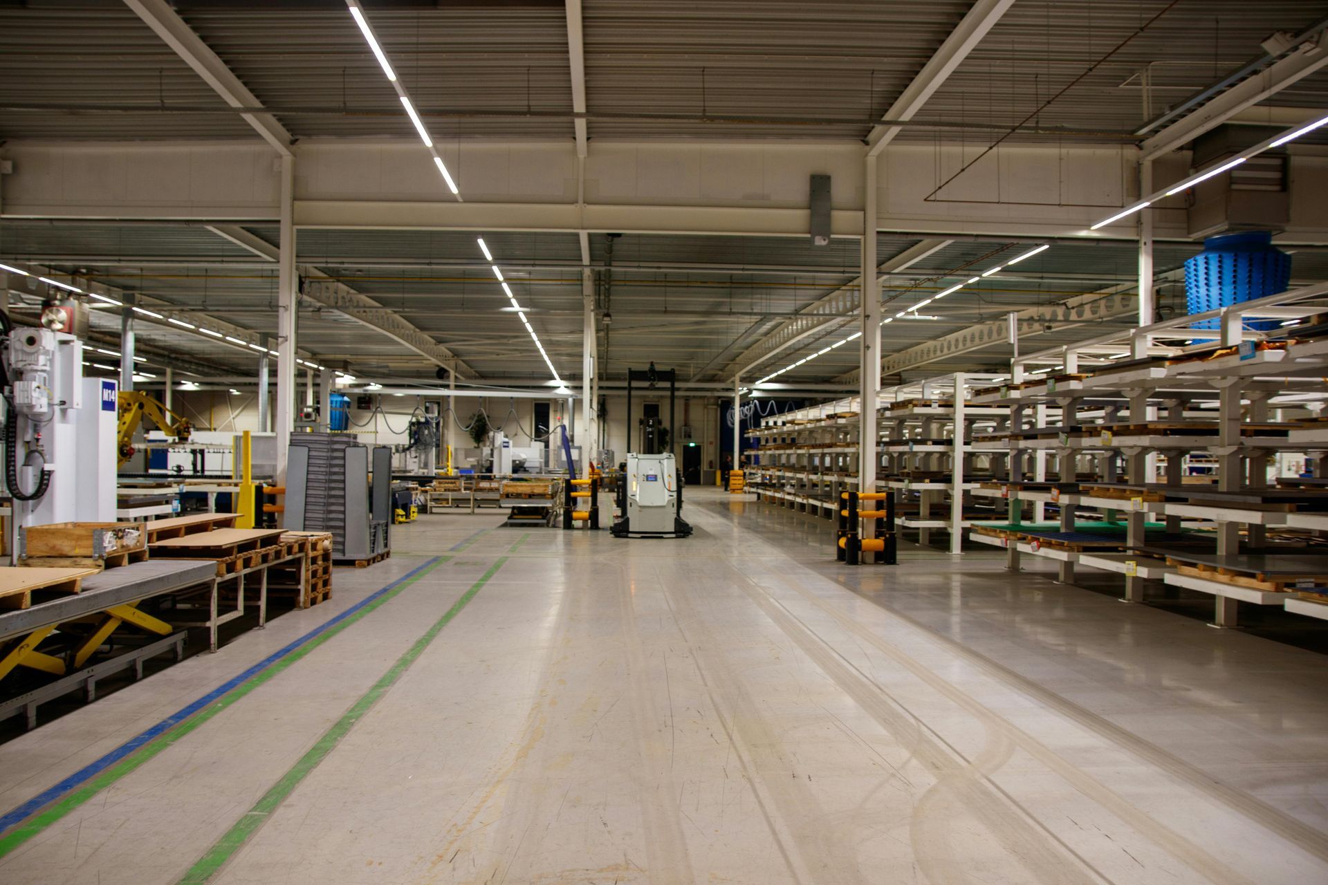 Large industrial warehouse aisle with conveyor belts, metal shelving, and a high ceiling under bright lights