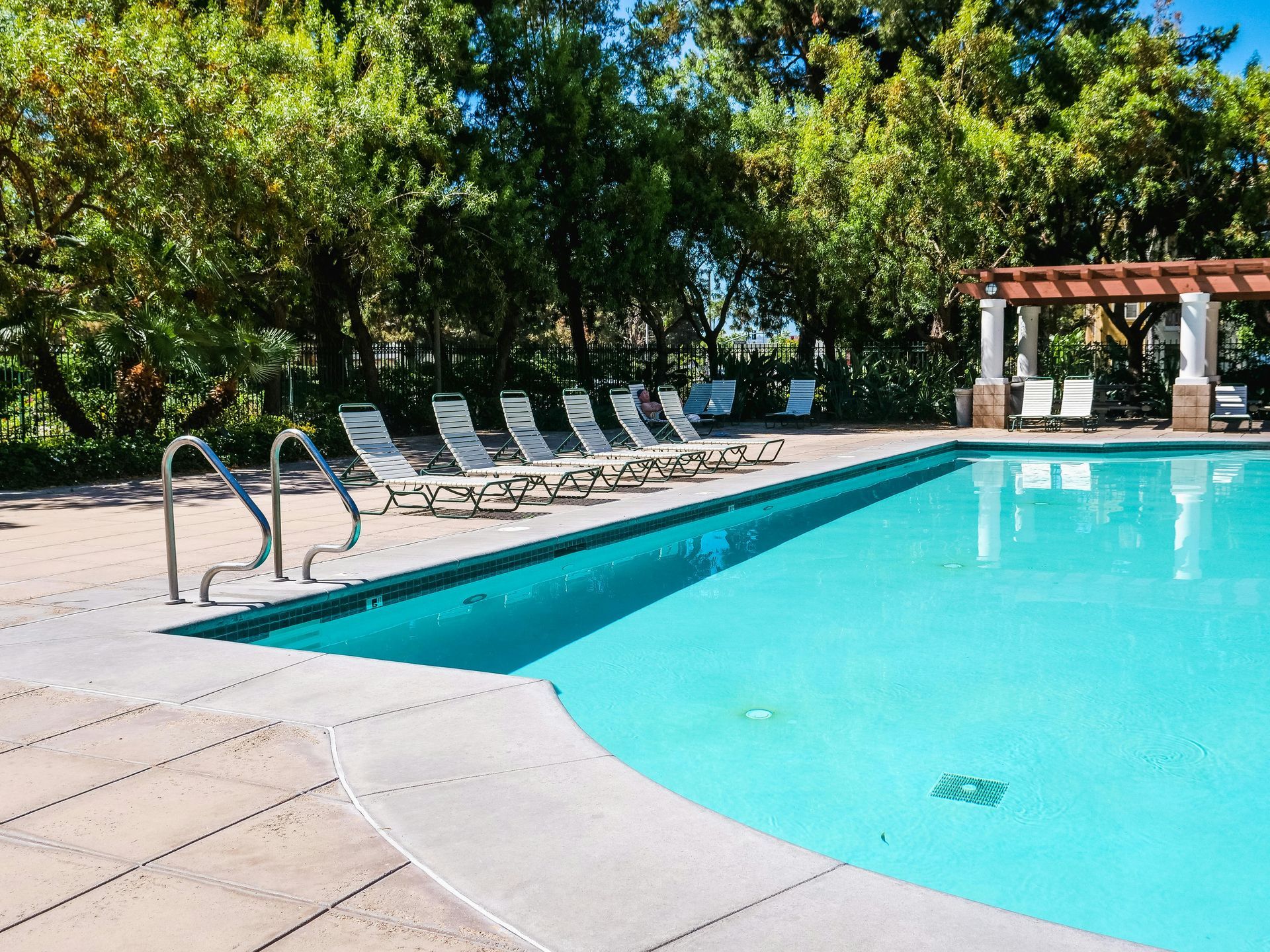 Outdoor swimming pool with turquoise water, lounge chairs, and a pergola surrounded by trees
