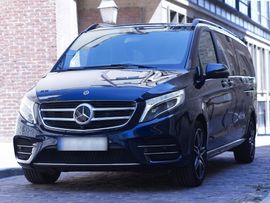 Un homme en costume aide une femme en robe à sortir d'une voiture noire. En extérieur.