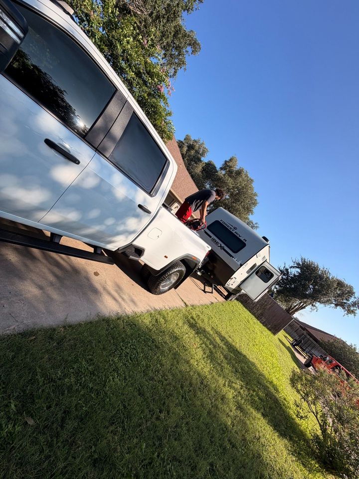 White pickup trucks parked on a sunny street, with a person standing near one and a grassy lawn in front.