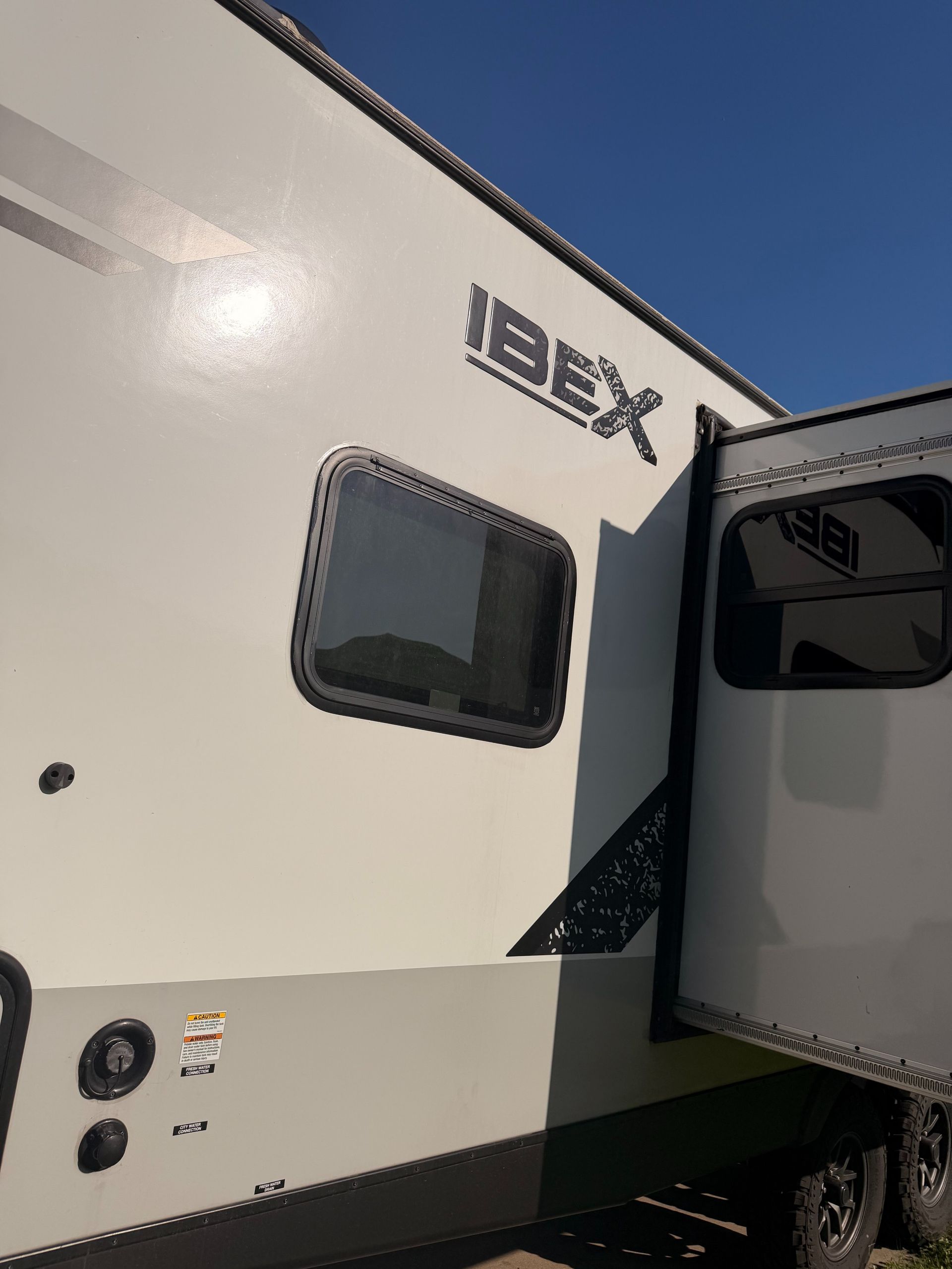 White IBEX camper trailer with windows and open door parked outdoors