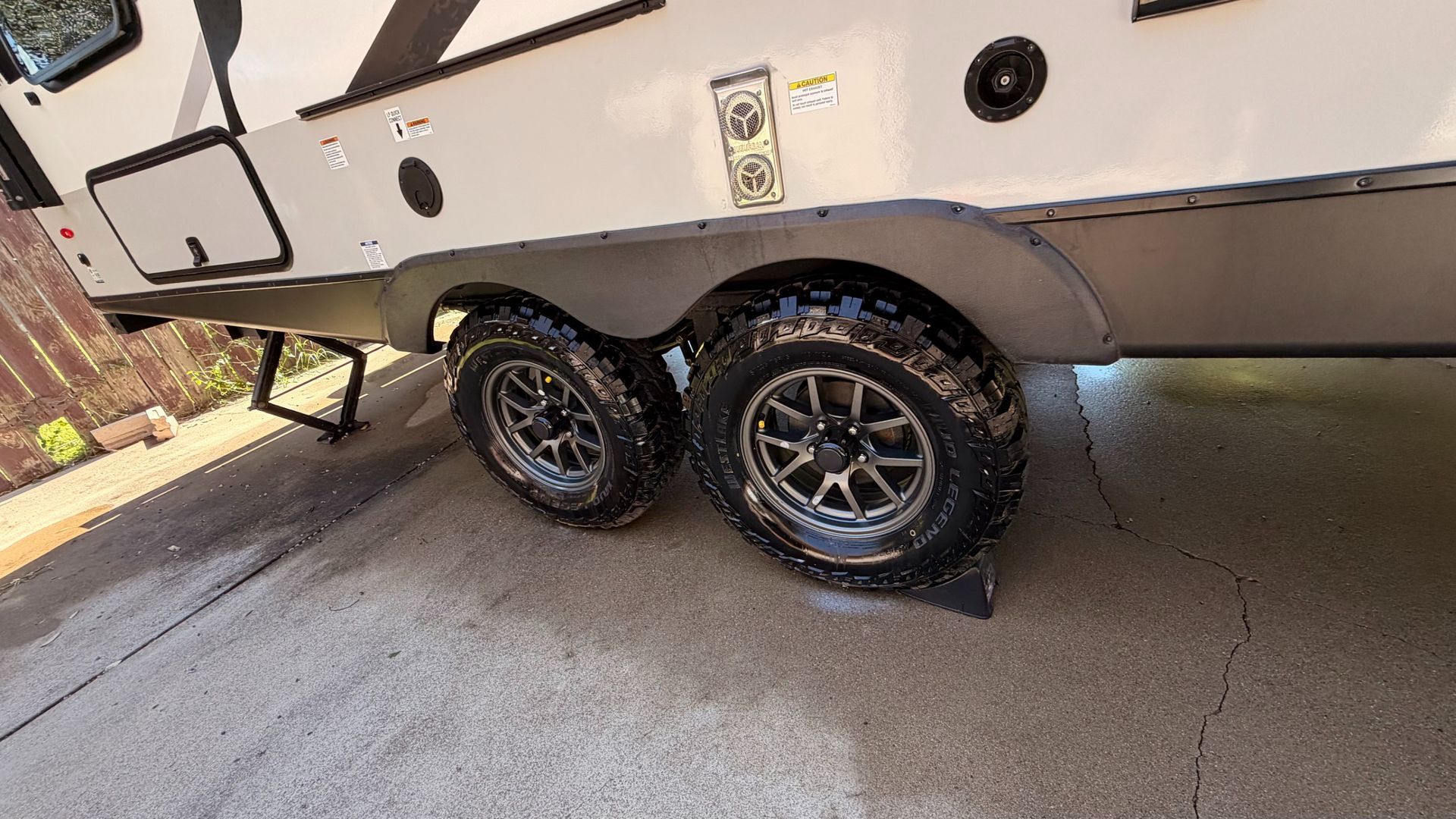 Two black off-road trailer tires under a white RV on a concrete driveway