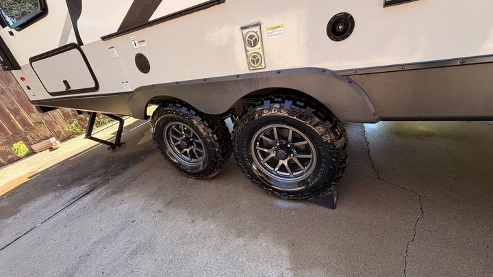 Two black off-road trailer tires under a white RV on a concrete driveway
