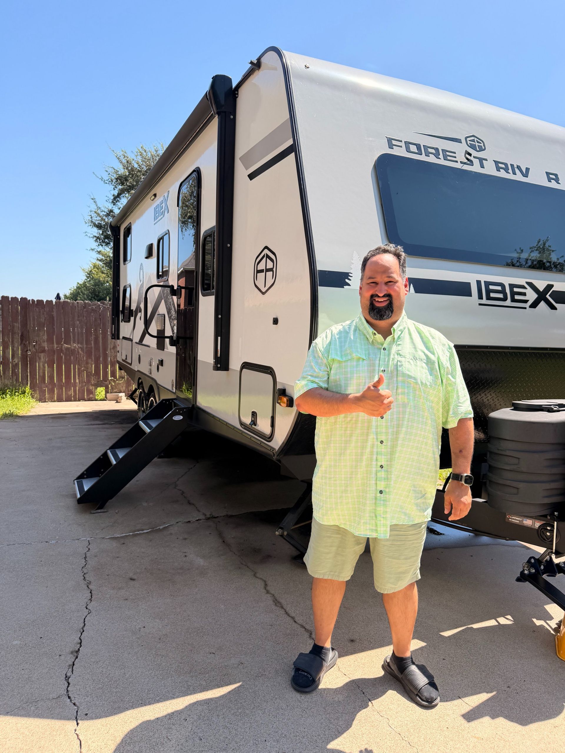 Man standing beside a white IBEX RV with black trim and open steps in a sunny driveway