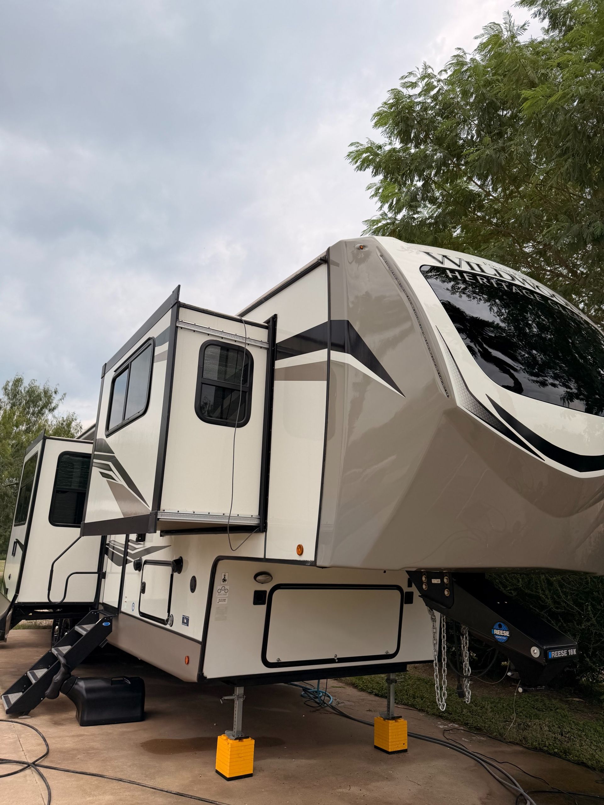 Large beige fifth-wheel RV trailer parked outdoors, supported by bright yellow stabilizers.