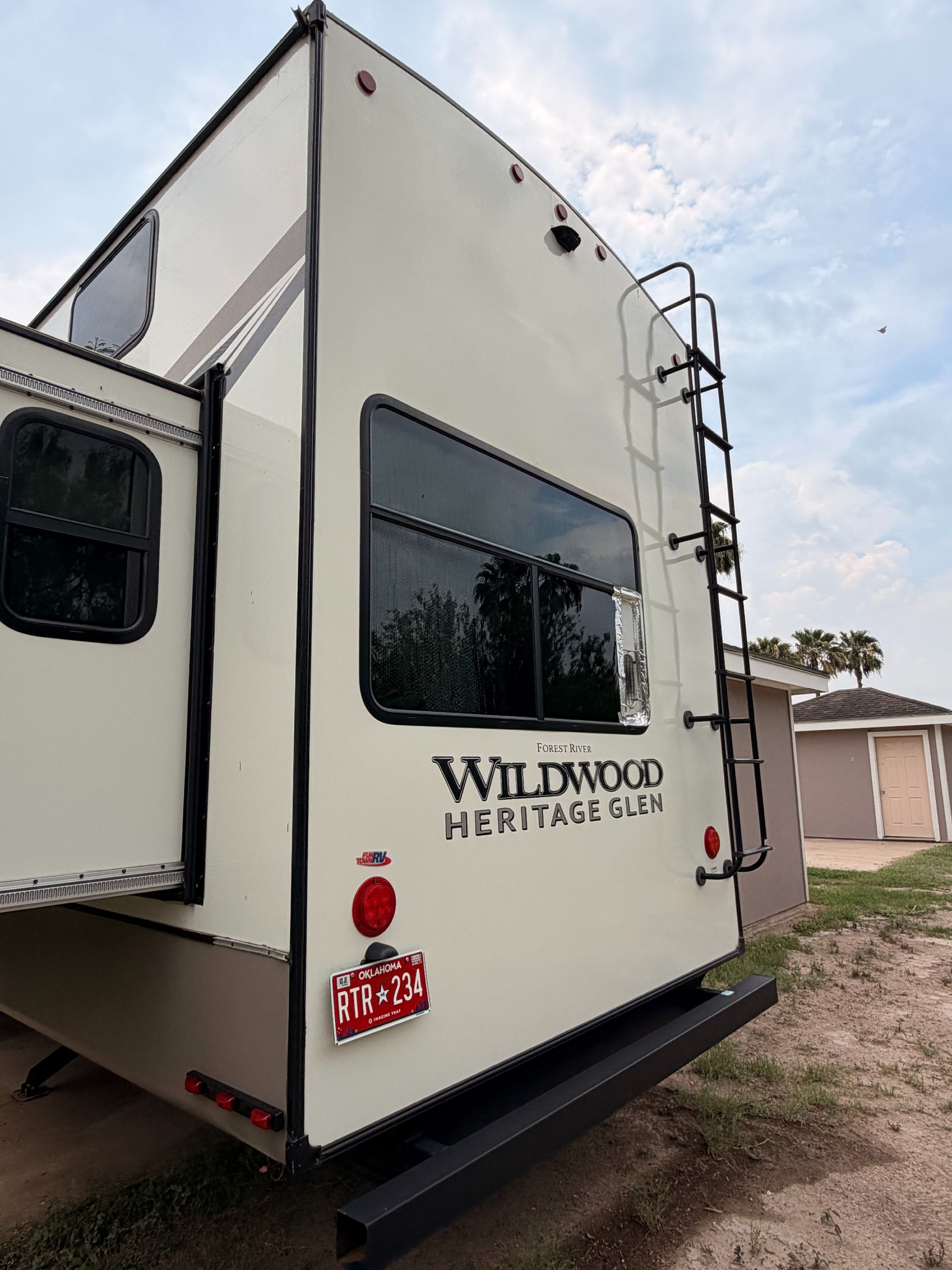 White Wildwood Heritage Glen travel trailer parked outdoors on gravel, viewed from the rear corner.