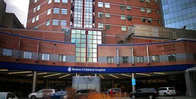 Boston Children's Hospital exterior with red brick, glass, and entrance with a sign. Cars parked outside.