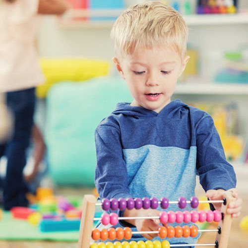 Boy with blond hair, using an abacus, indoors. He is looking down intently.