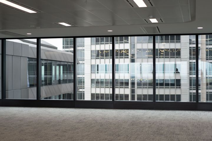 Modern open office with wooden desks, black chairs, glass walls, and ceiling strip lighting