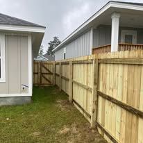 Wooden fence between two houses; green grass, cloudy sky.