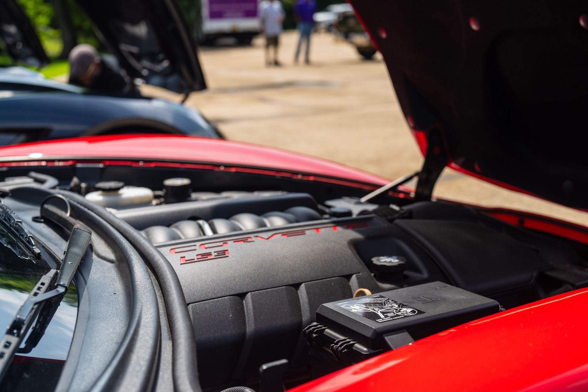 Close-up of a red Chevrolet Corvette's engine bay with the hood open at an outdoor car show.