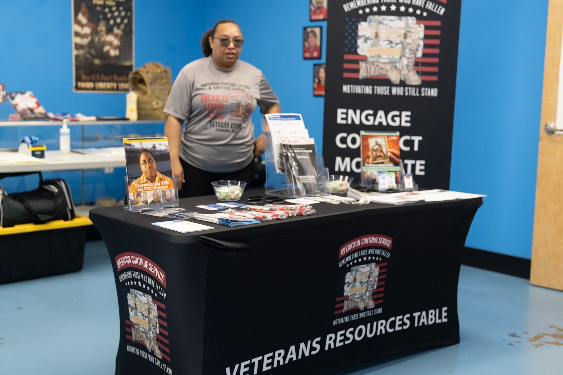A person stands behind a Veterans Resources Table display with educational materials in a blue-walled room.