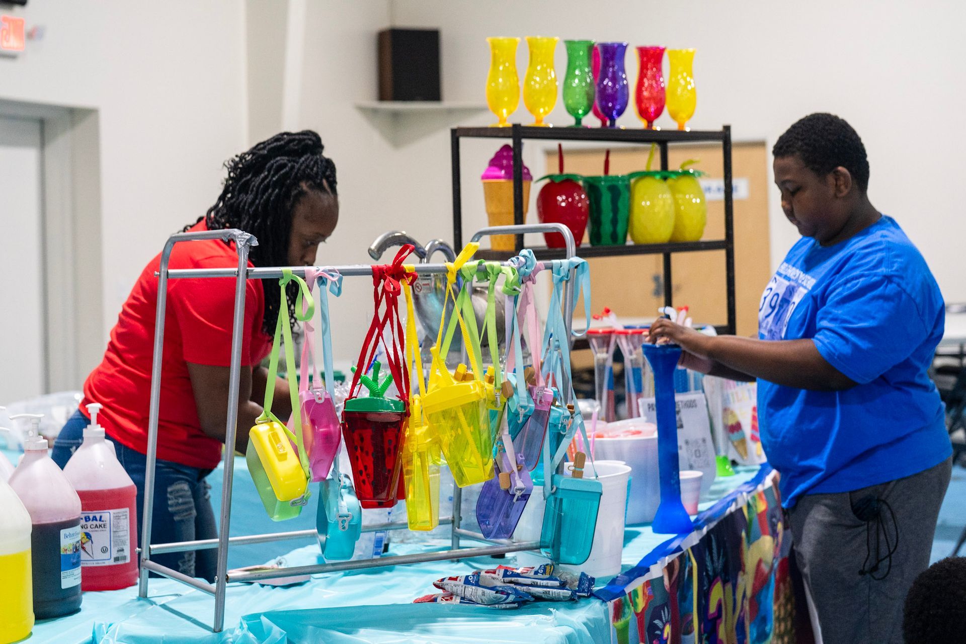 Two people setting up a colorful party drink station with bright plastic cups and containers on a table.