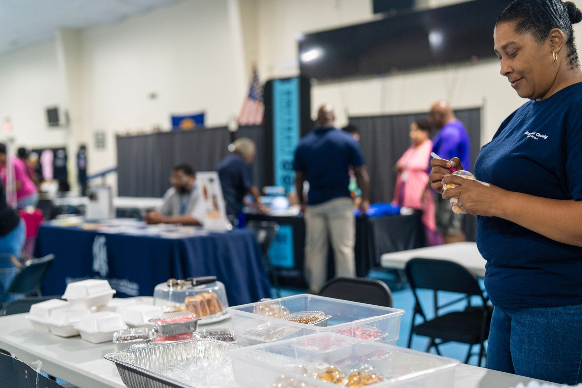 People gather at tables in a brightly lit hall, with one person in the foreground looking at a snack.