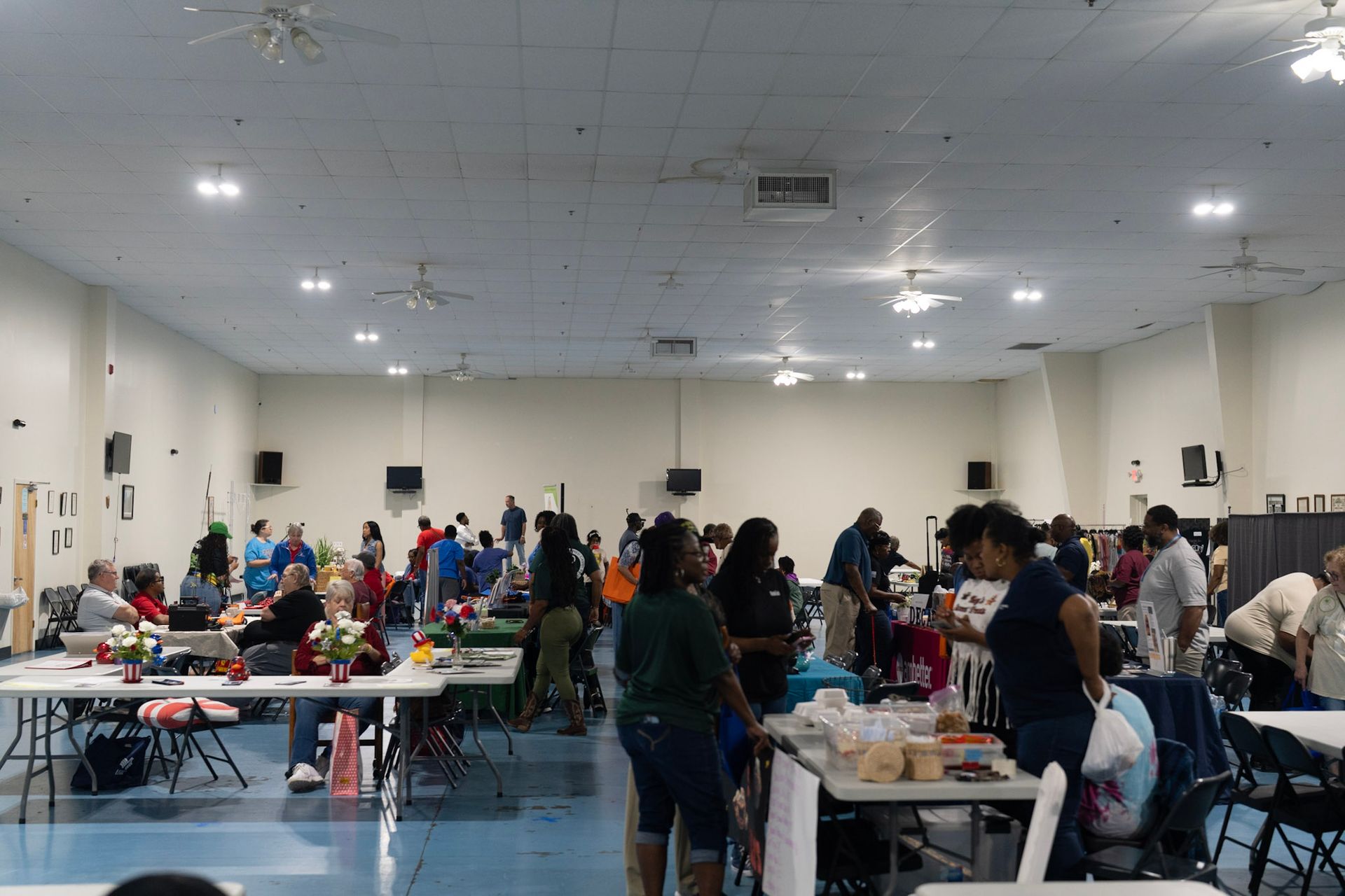 A spacious, well-lit hall with people gathering around several tables for a community or social event.