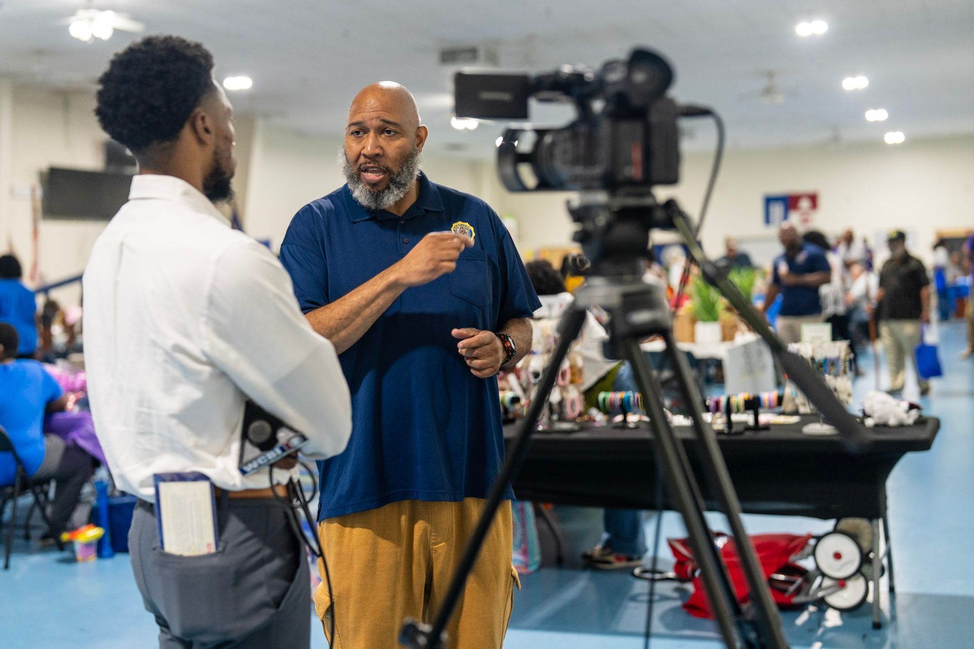 A videographer films a conversation between two people in a large, bright community space.