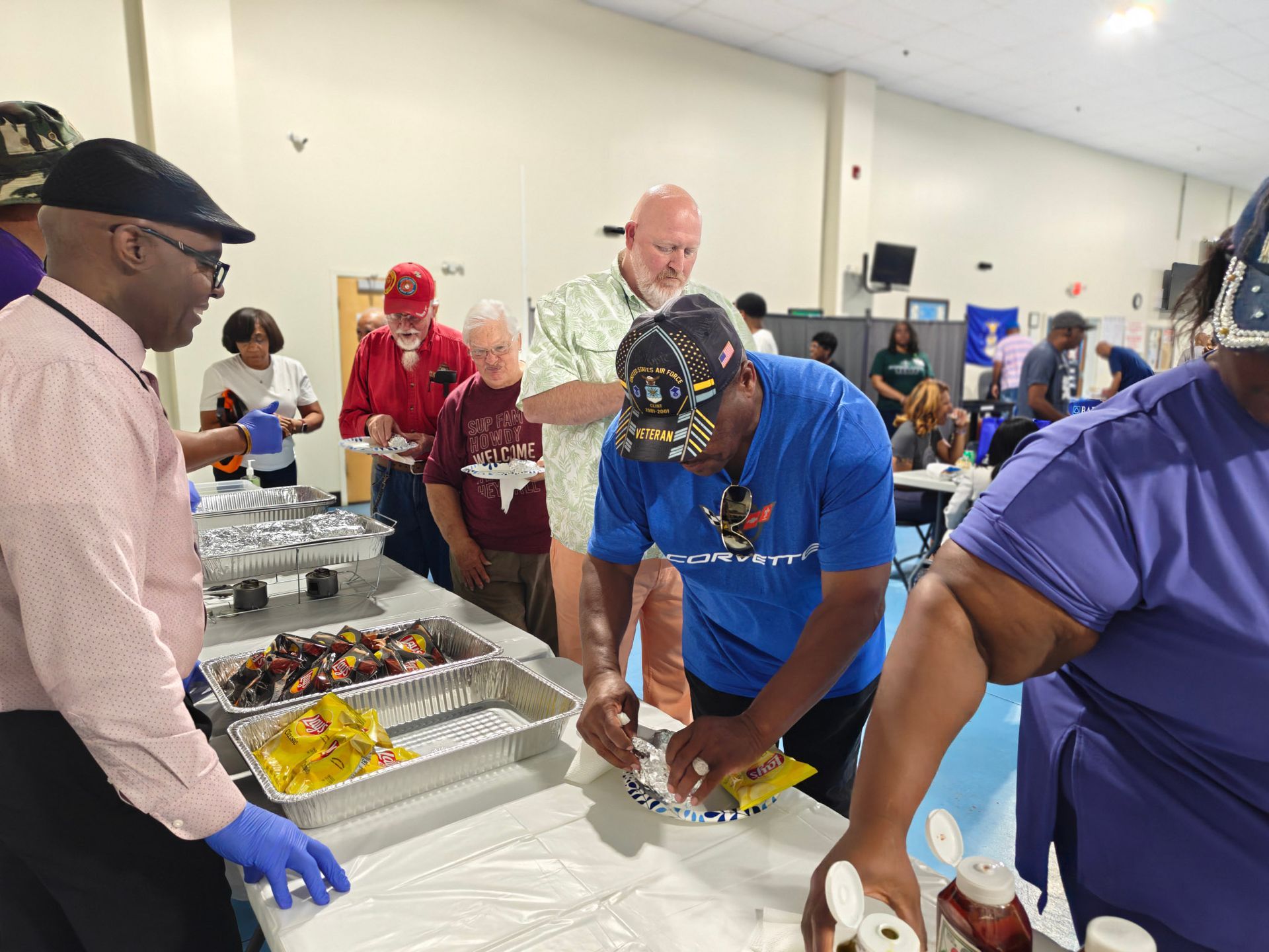 People serving food at a buffet table in an indoor gathering space.