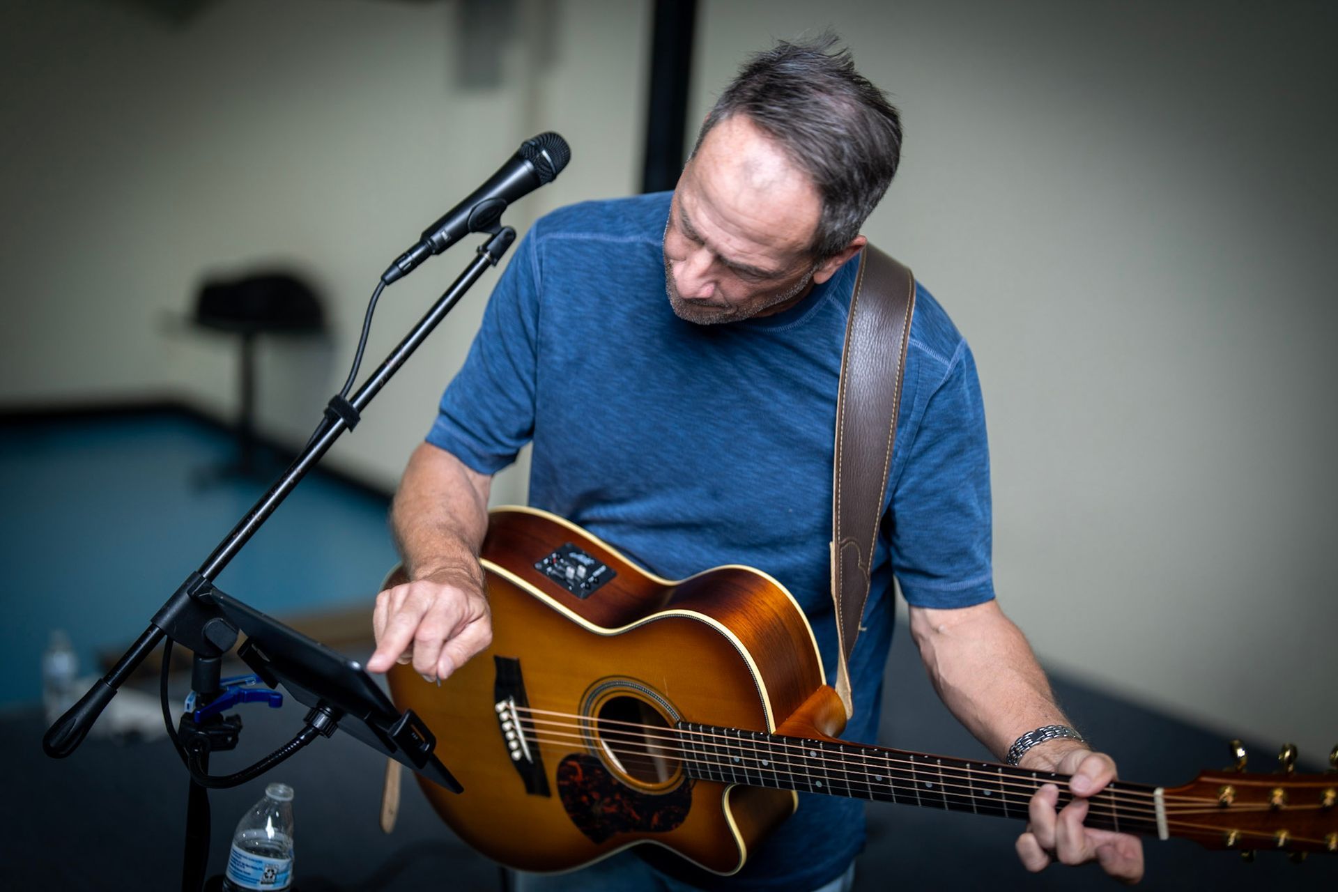 A person in a blue t-shirt plays an acoustic guitar while performing into a microphone.