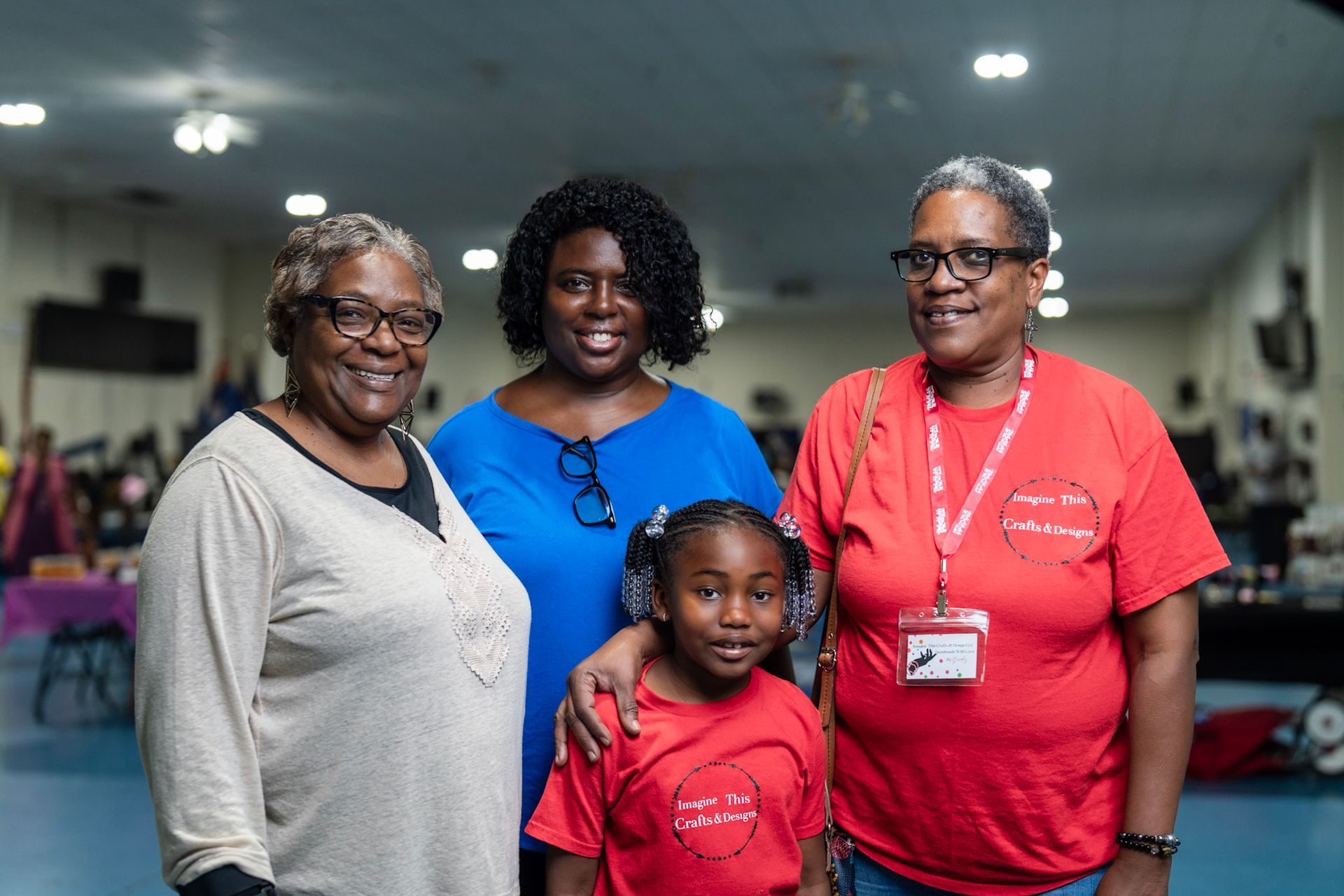 Four people stand close together in a hall, smiling at the camera. Two wear red shirts, one wears blue, and one wears beige.