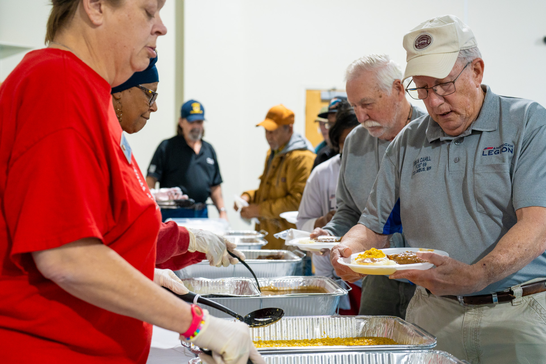 A woman in a red shirt is serving food to a group of people.