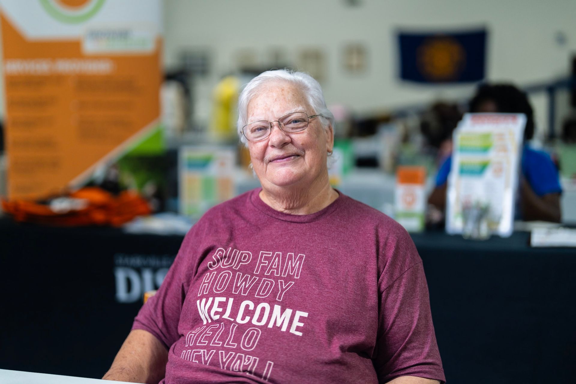 A smiling person wearing a maroon shirt with the word 