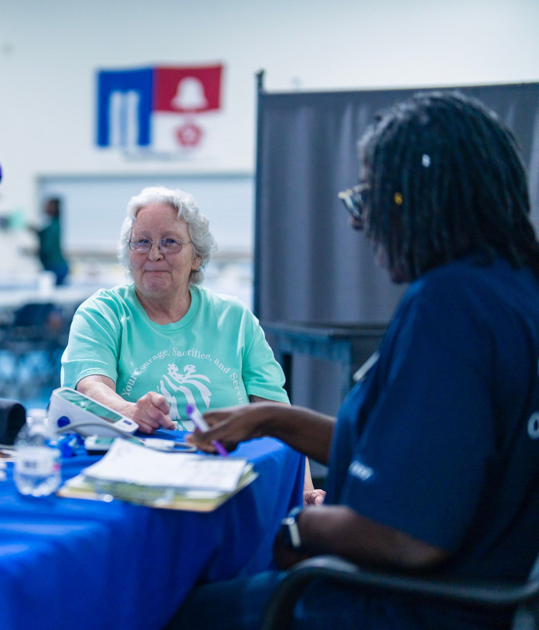 A person in a light green shirt has their blood pressure checked by a professional at a table with a blue tablecloth.