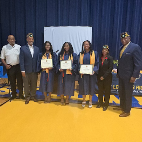 Eight individuals stand on a yellow stage in front of a blue curtain, with three students holding certificates.