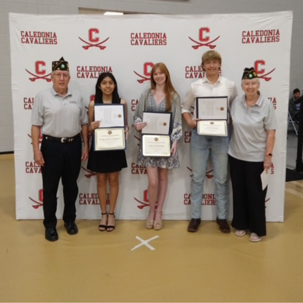 Five people stand smiling in front of a Caledonia Cavaliers backdrop holding certificates at an awards ceremony.