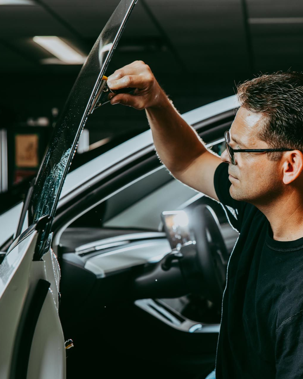 Man applying tint to a car window inside a shop.
