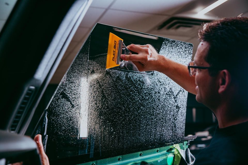 Person applying tinted film to a car window with a squeegee.
