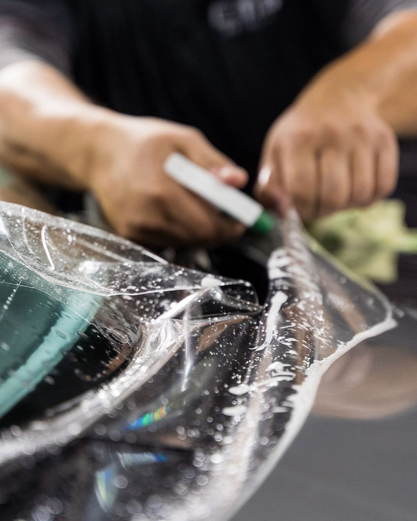 Person using a pen to trim clear plastic film, likely for window tinting.