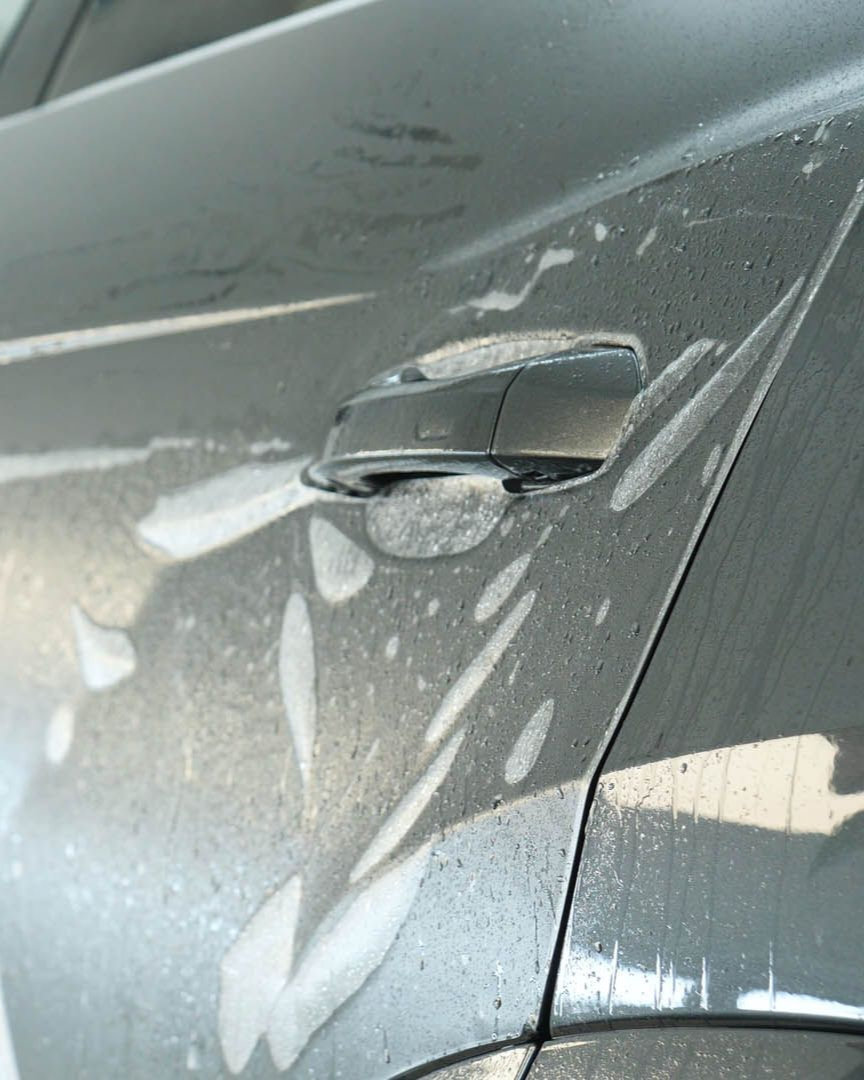 Car door handle covered in soapy foam during a car wash. Gray car, silver handle.