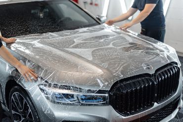 Person in black gloves polishes a car with a red and black power buffer in a garage.