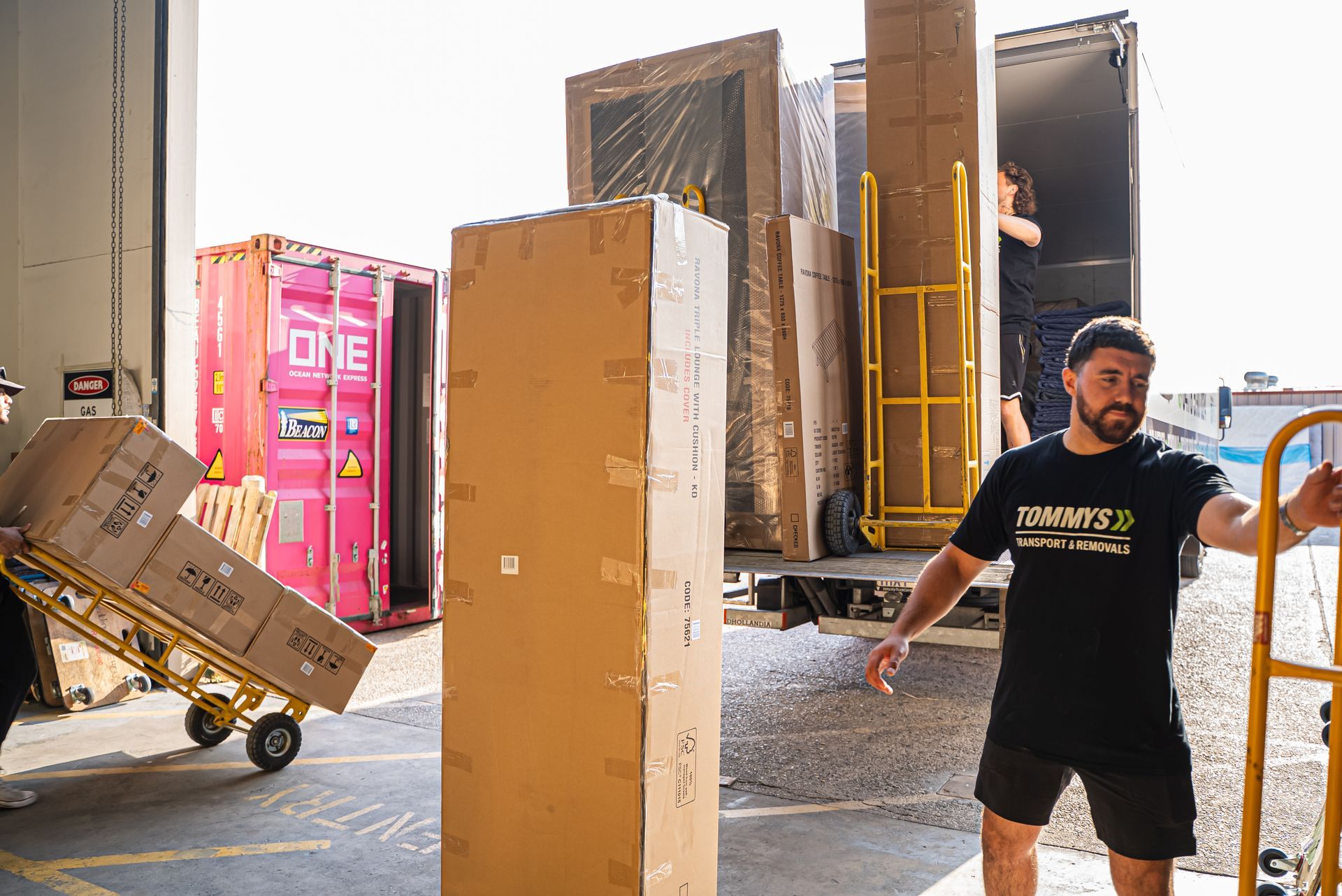 Removalist in black shirt unpacking cardboard boxes into a warehouse loading area.