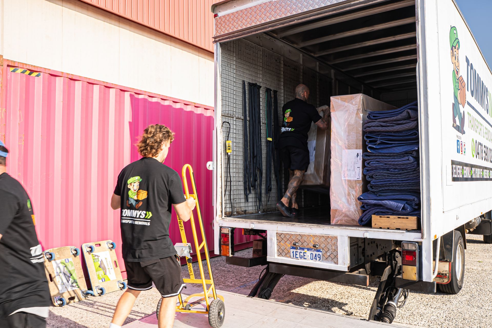Workers unload boxes from a delivery truck beside a pink shipping container.